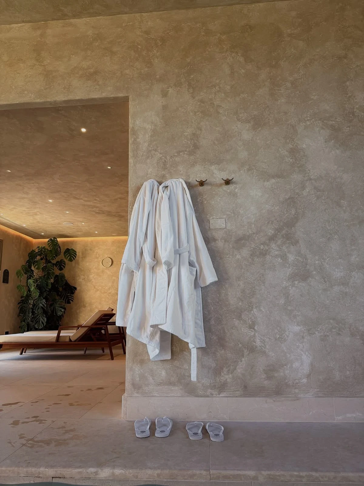 Two white bathrobes on a stone wall in a quiet spa, slippers waiting below