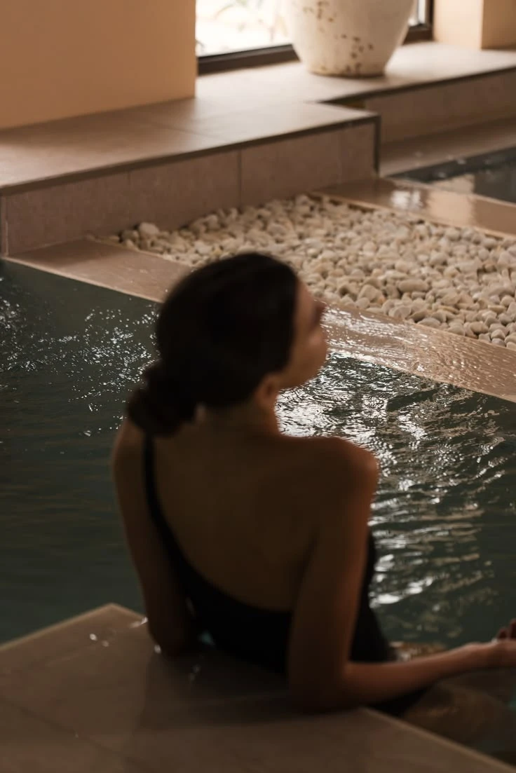 Woman relaxing in a calm indoor spa pool, seen from behind